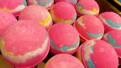 Display of pink Lush bath bombs with swirls of blue, white and yellow across the middle of the sphere shaped item.
