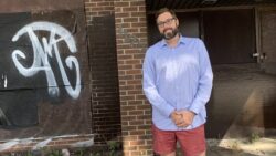 Shawn Menard stands in front of a brick building with graffiti.
