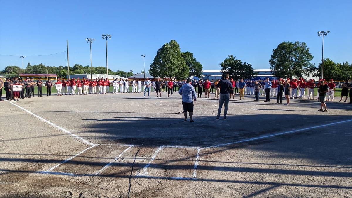 Players line up along the edge of the fast pitch softball infield while watching guest speakers.