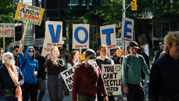 Climate activists march through the streets of Ottawa holdings signs that spell "vote."