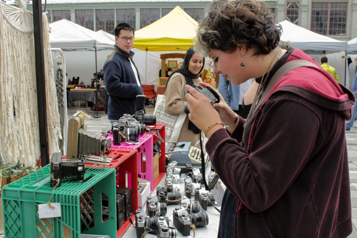 Neddy McIntyre looking at a film camera while people walk by and watch