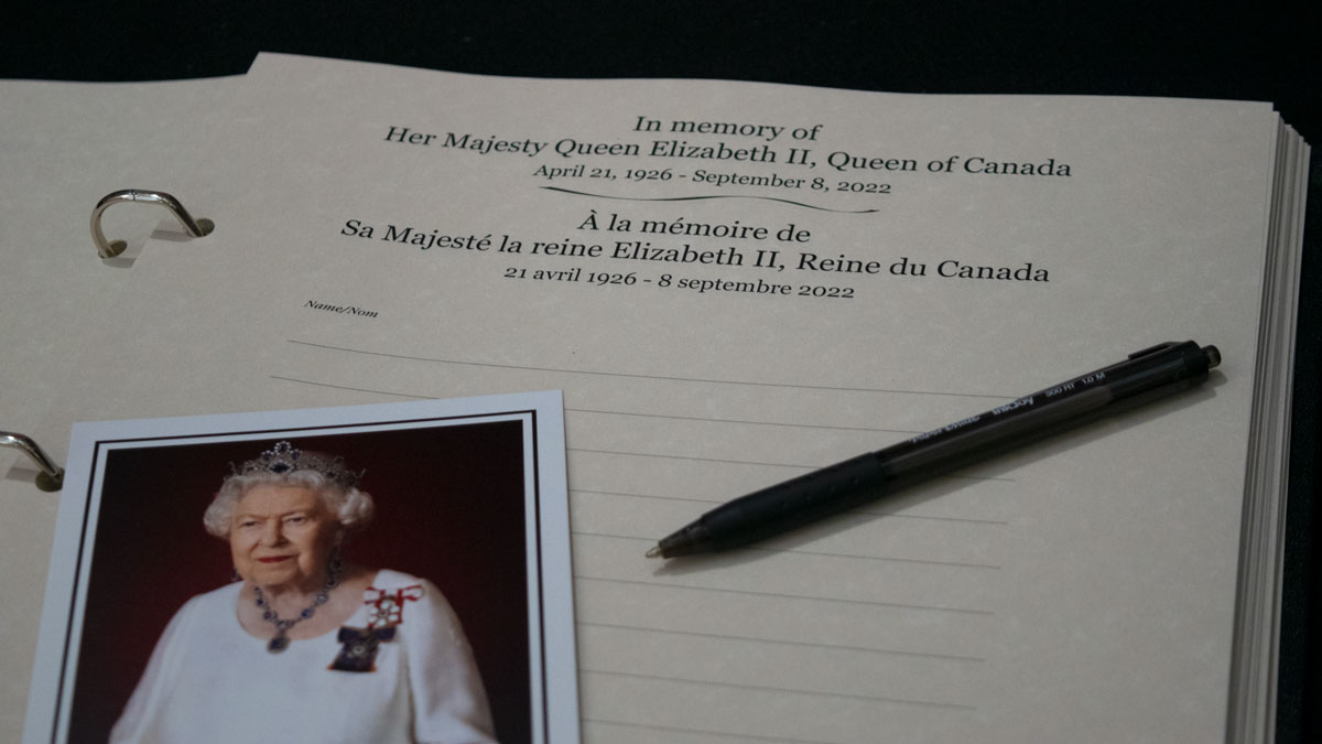An open book with the page titled, "In memory of Her Majesty Queen Elizabeth II, Queen of Canada" and a pen and photograph of the Queen laid on it.