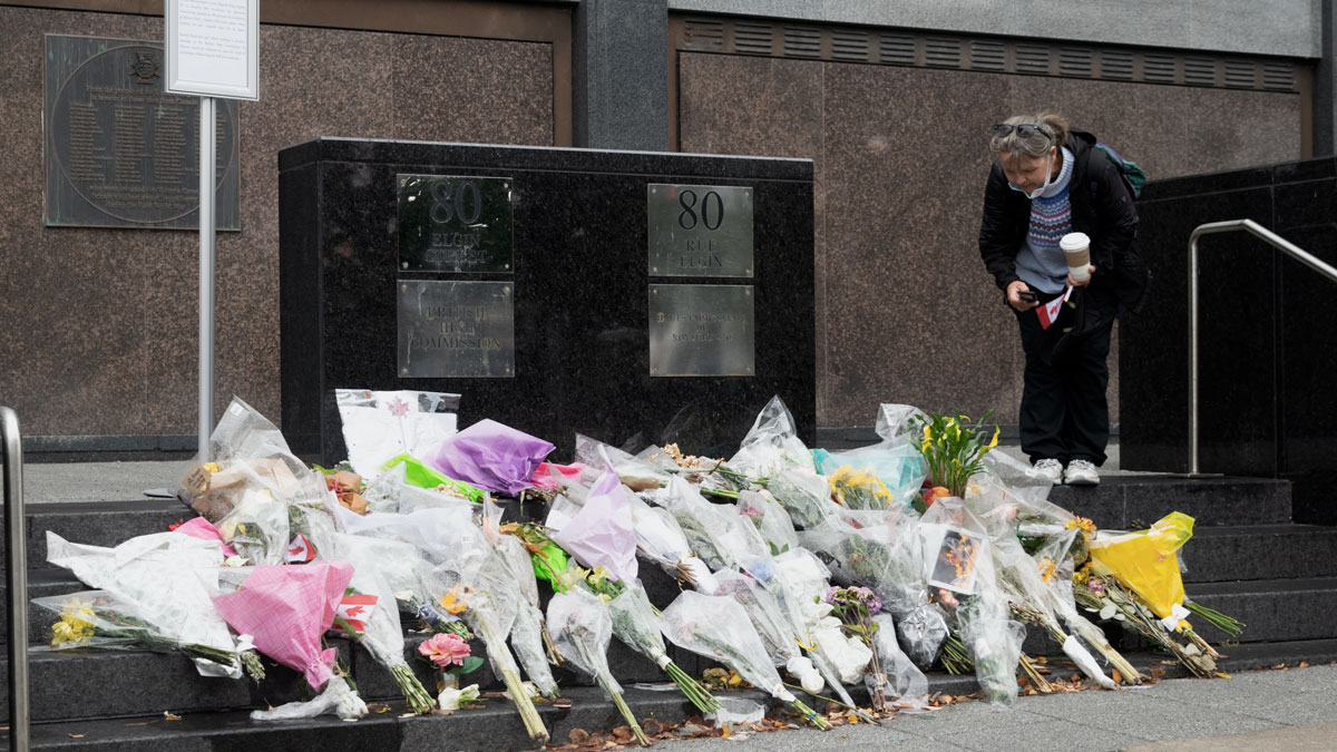 A woman peers over the pile of flowers laid on the steps of the British High Commission building in Ottawa.