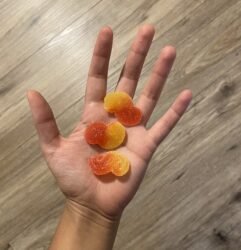An open-faced palm of a hand holding three yellow and red cannabis gummies.