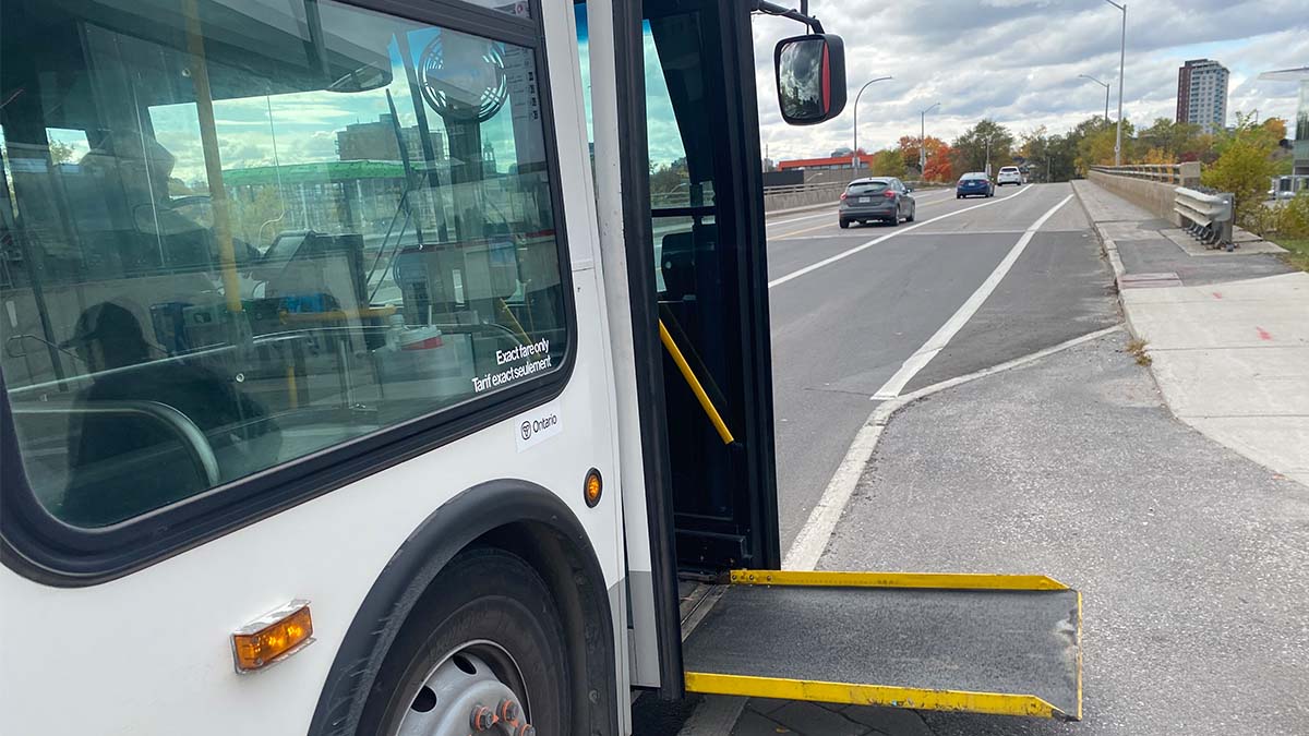 An OC Transpo bus sits at a stop with its wheelchair ramp extended. Ramps and level boarding make transit more accessible.