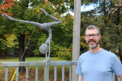 Chris McGuffin standing beside his wire gymnast sculpture.