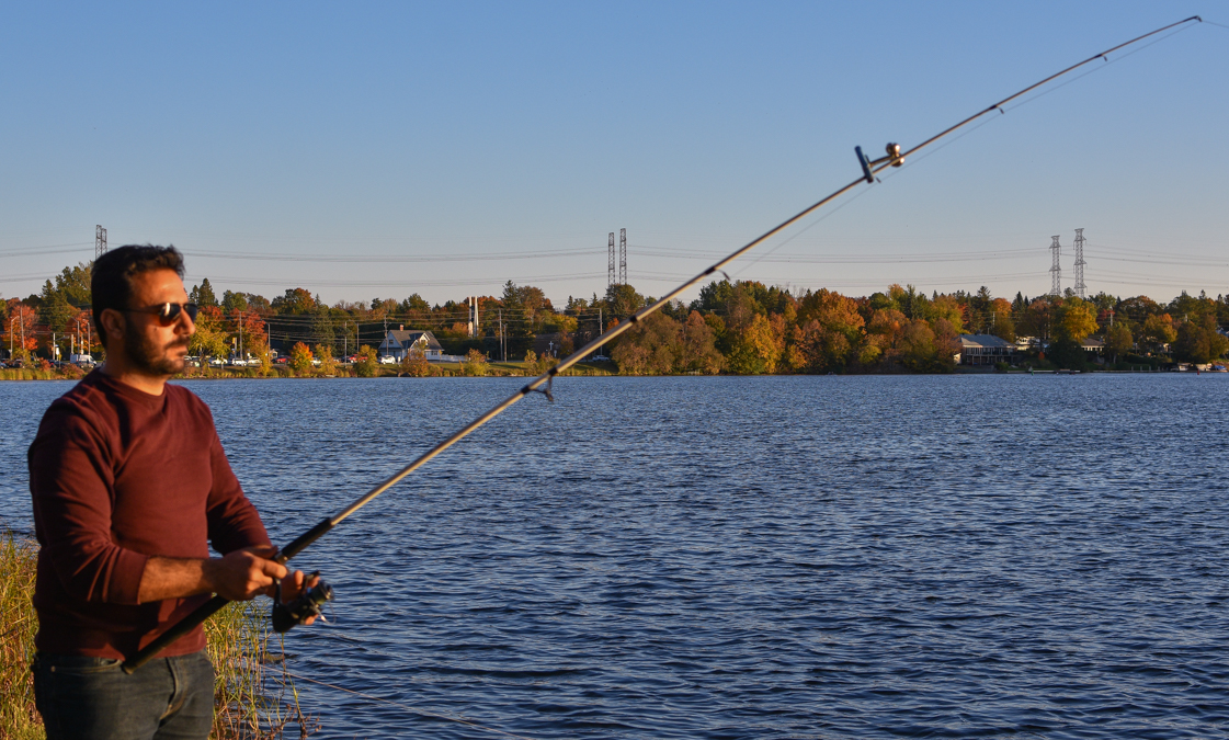 Man holds fishing rod and looks out over the Rideau River