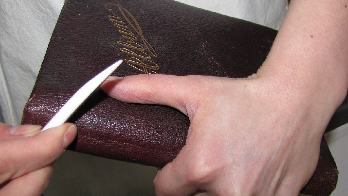 Two hands working on repairing the binding of a book.