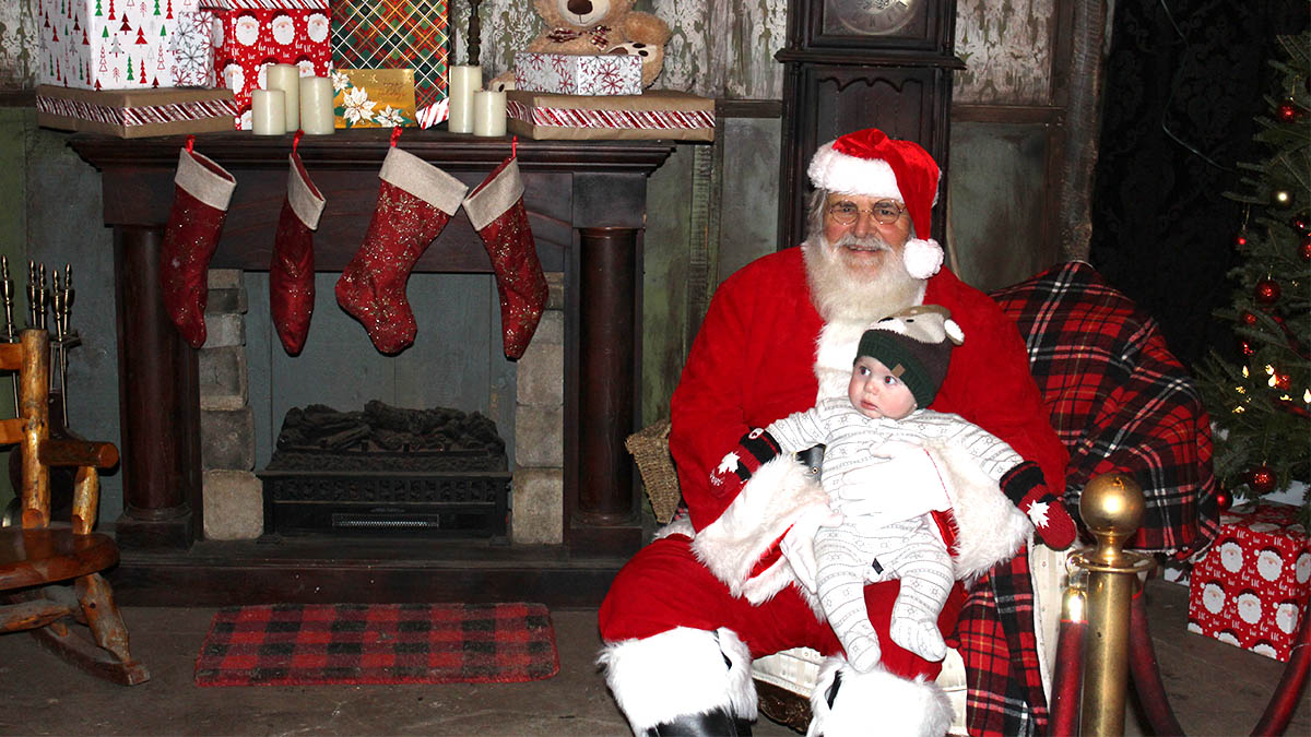 Santa sits in front of a fireplace with a young child on his lap
