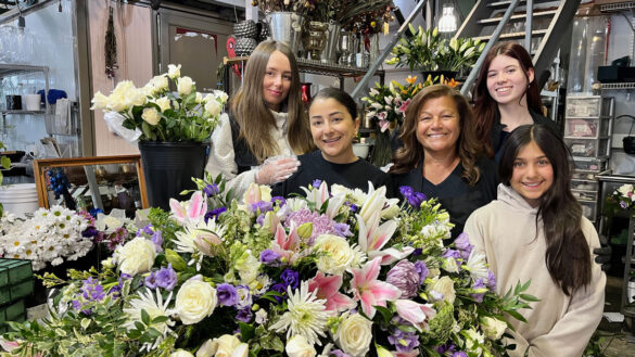 Five people standing in front of bouquets of flowers