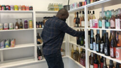 Benson Mutalemwa, CEO and founder of Knyota Drinks, organizes drinks on a middle shelf inside his store. [Photo @