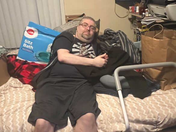 Justin Saunders sitting on his bed surrounded by donated items.