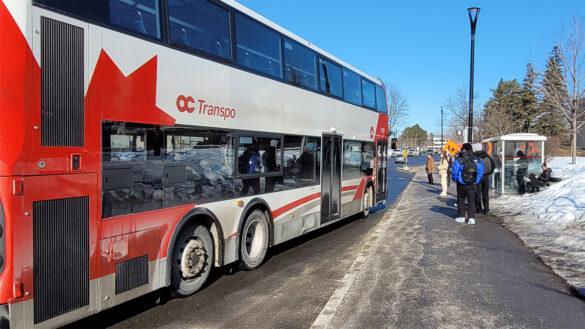 An OC Transpo bus pulls up to a curb to take on passengers. The transit commission recently approved a yearly budget that relies on a hoped-for $39-million in funding from the Ontario government. Critics question the assumption that the provincial money will come through, arguing the city should have raised taxes to cover the shortfall rather than risk a potential cut to services. [Photo © Gabrielle Huston]