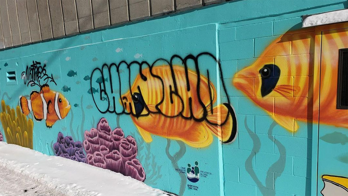A mural with fish painted on it. Two graffiti tags sprayed on top of it.