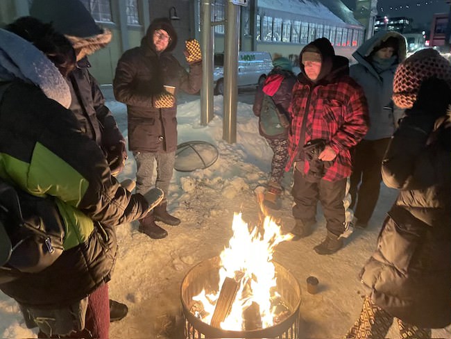 Howard Adler warming up around the fire pit while holding a cup of hot chocolate alongside moviegoers. [Photo © Wafa El-Rayes]