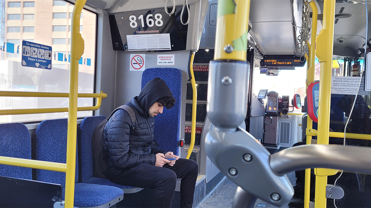 A man sits on a public bus, scrolling on his phone.