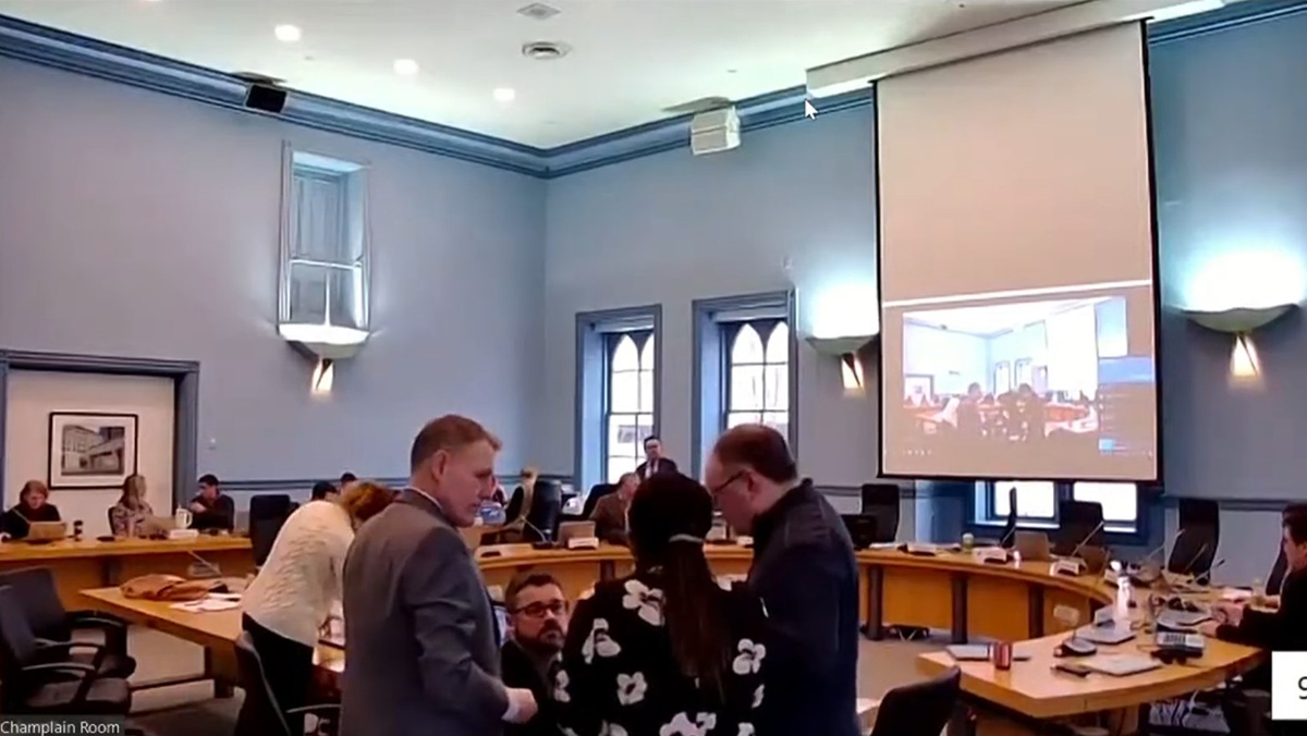 A large board room with a round table and scattered people.