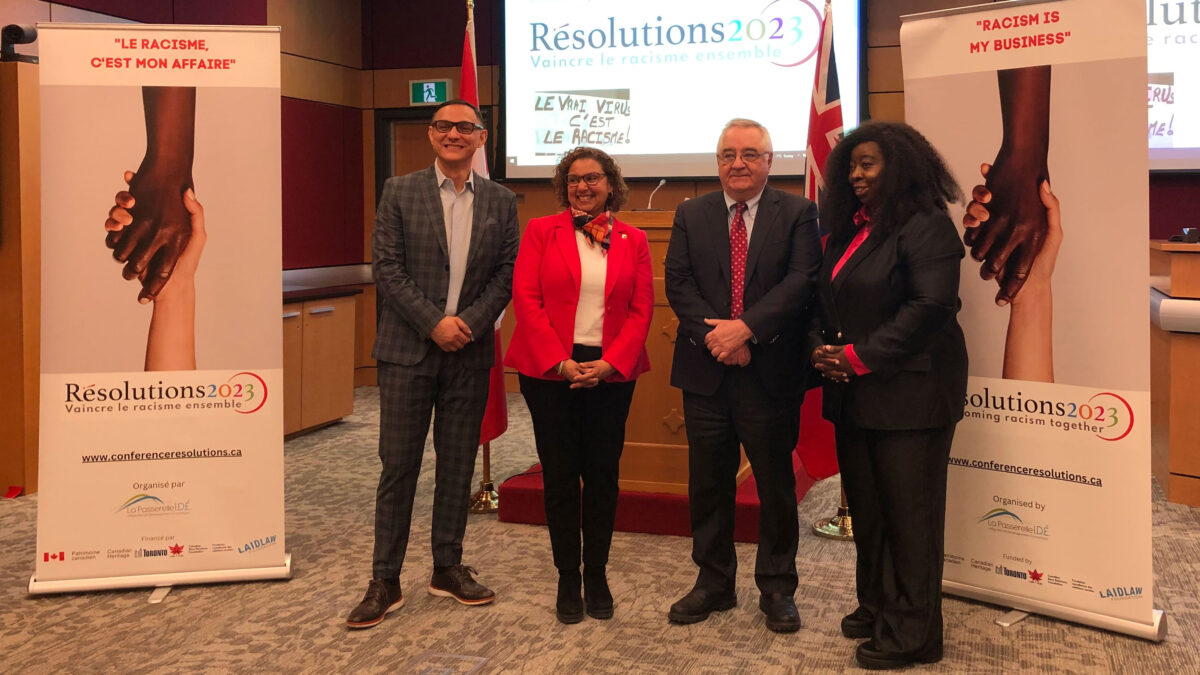 (Left to right) Mohamed Boudjenane, Senator Bernadette Clément, Ronald Bisson and Leonie Tchatat stand between two of the conference signs that say "Racism is my business" with hands reaching across.