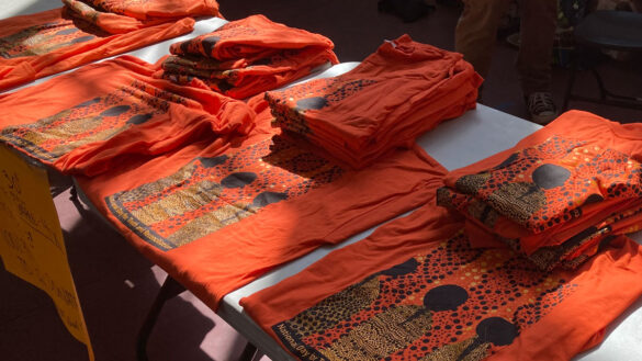 Stacks of orange shirts that read "National Day for Truth and Reconciliation" are laid out on a grey table.
