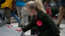 A young girl wearing a dark green jacket and a pinned paper poppy places a legion poppy on the Tomb of the Unknown Solider after the National Remembrance Day Ceremony on Nov. 11, 2023.
