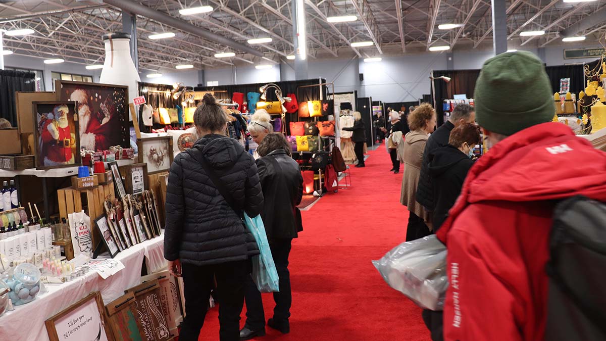 Group of people looking at booths at the Nepean Sportsplex Christmas Market. There are paintings, bags and other handmade goods on display.