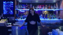 Meghan Glennie wears black leggins, a t-shirt, and zip-up and is smiling in front of a stocked bar. She is the manager of The Lookout Bar in ByWard Market.