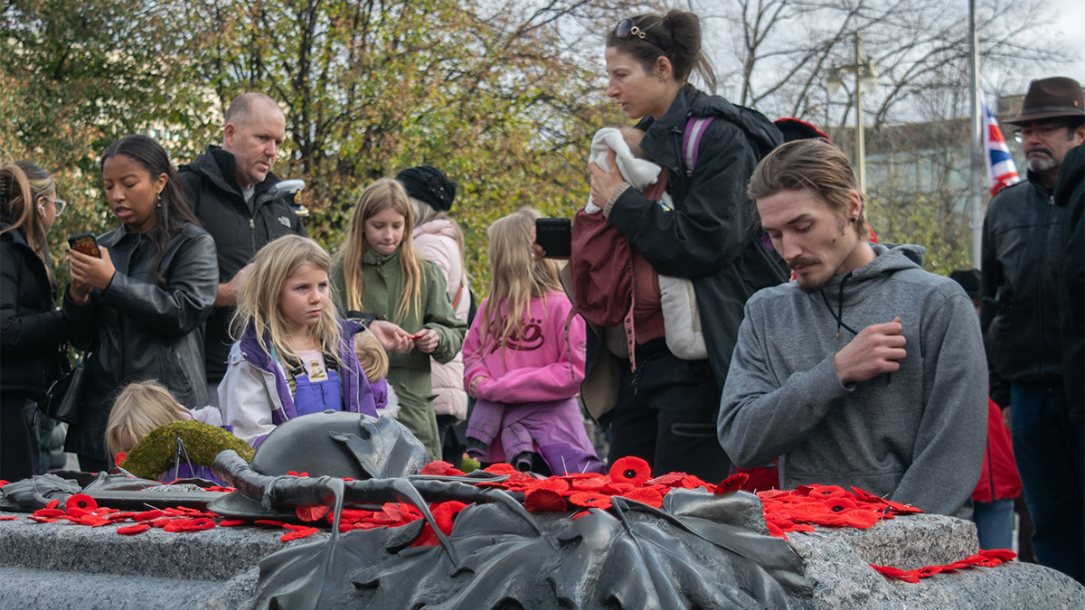 A young child curiously observes as a man as he lays his poppy and places his hand on his chest kneeling beside the Tomb of the Unknown Solider in Ottawa Ont