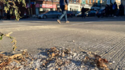 A pile of de-icing salt on the sidewalk with people walking in the background.
