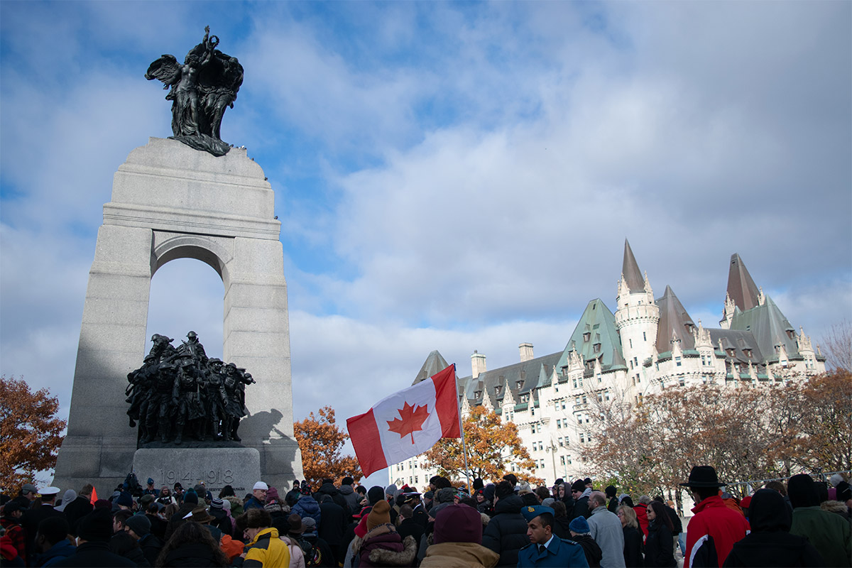 Over a crowd of people and a waving Canadian flag, Sunlight illuminates part of the Tomb of the Unknown Solider in Ottawa Ont.