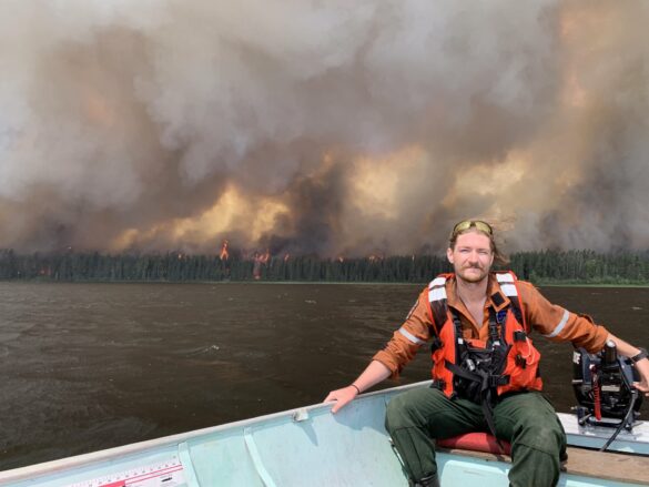 Eric Davidson is seen here on a boat as a wildfire rages in the distance. He says more firefighters are needed to be ready another wildfire season.