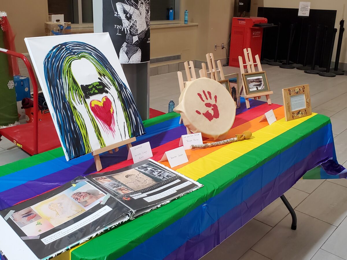 Several multi media art pieces on a rainbow coloured table. 