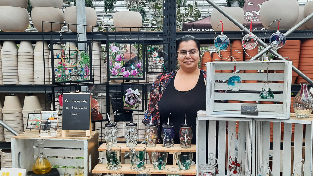 Sarah Ladhani, owner of the small business Just a Thought, standing with her hand-painted glassware at her vendor at the Rober Plante Greenhouse winter Market.