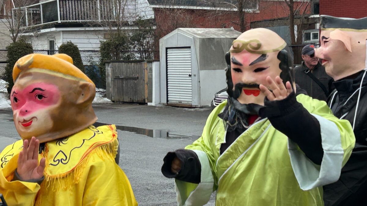 Two people wearing decorative masks wave at people on the sidewalk.