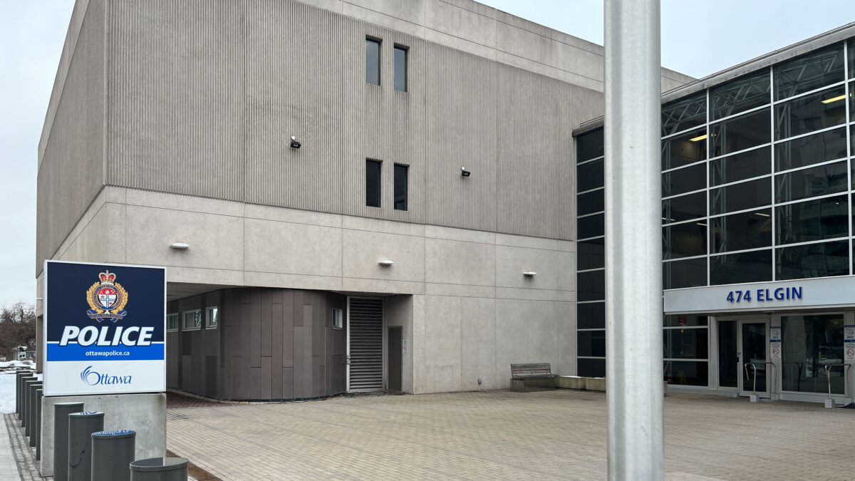Photo of outside of Ottawa Police Service 474 Elgin headquarters. OPS sign is visible in the bottom left of the photo and the address of the headquarters is displayed to the right of the photo.
