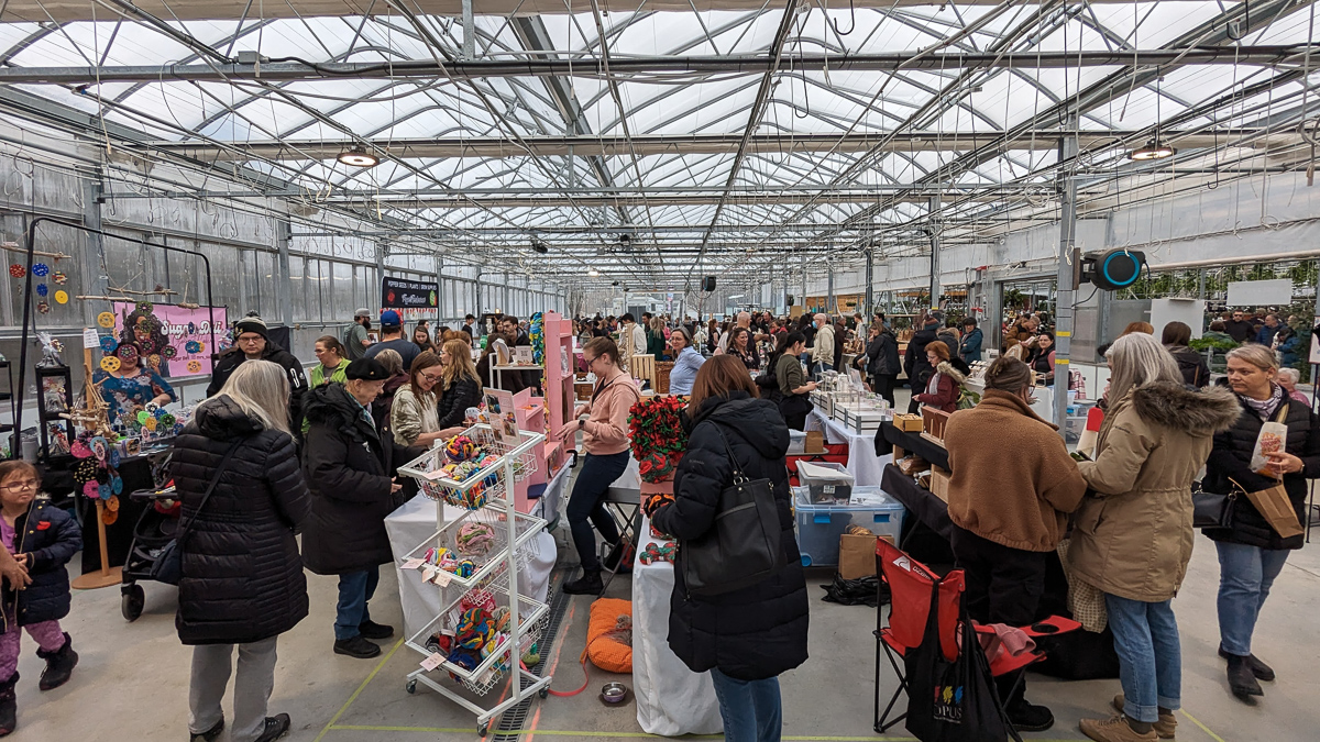 Large greenhouse full of dozens of vendors and shoppers.