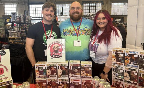 Two men and a woman smile standing behind a table filled with collectible figures at a recent gaming and comic collectibles event at Lansdowne Park