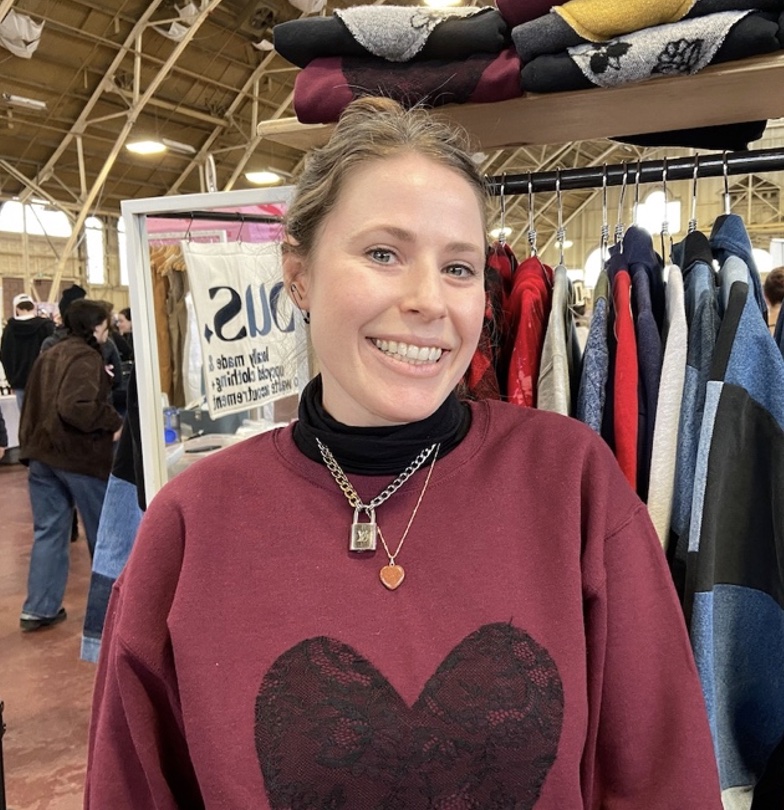 smiling female vendor poses wearing sweater with heart
