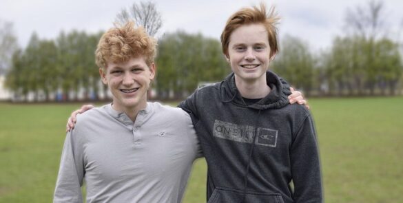 Two male high school students stand beside each other smiling in a school field