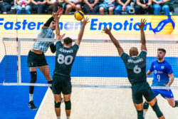 Two Canadian volleyball players preparing to block an incoming strike from an Argentinian player.