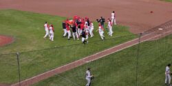 A dozen baseball players converge to celebrate a win between first base and the pitcher's mound at Ottawa Stadium