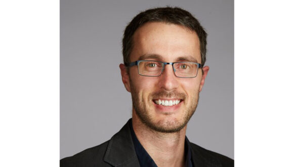 Allan Reesor-McDowell smiling in front of a grey background.