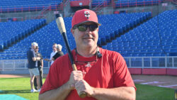 Bobby Brown poses with a baseball bat on his shoulder. He is wearing a red shirt and a red Ottawa Titans baseball cap.