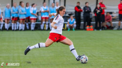 Photo depicts a woman in her soccer uniform. She is preparing to kick a ball while running on a soccer field.