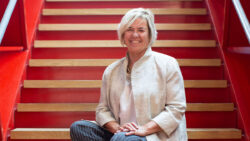 Julia Elvidge is seated on red stairs, smiling.