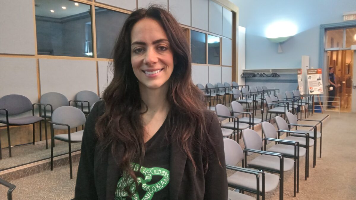 A light-skinned lady wearing a black jacket and an inner black top with a green design.