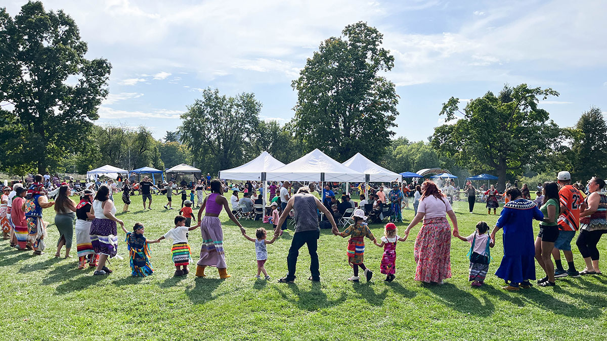 People holding hands in a large circle around a white tent.