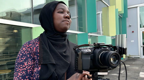 Amatur Rahman Salam-Alada poses behind a camera at Algonquin College