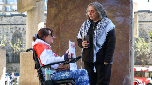 A woman wearing a Palestinian scarf speaks to a woman in a wheelchair holding a sign