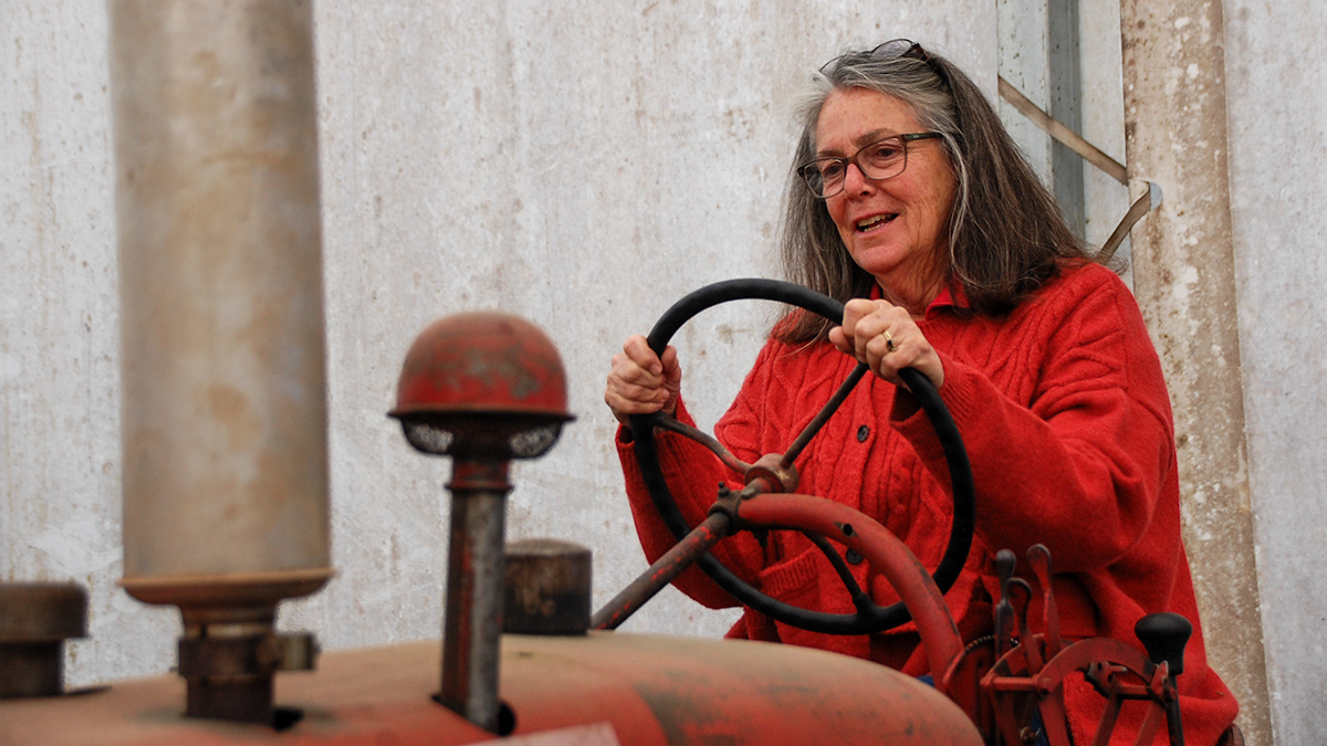 Shelley Lyall pretending to drive an old tractor inside a barn.