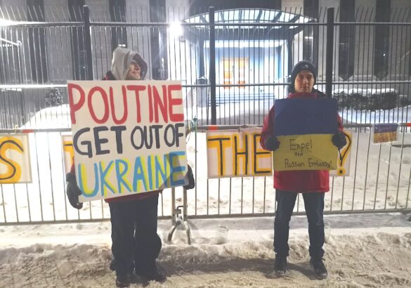 Two protesters hold signs in front of the gates of the Russian embassy in Ottawa.